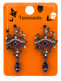 A pair of gothic-style Halloween dangle earrings displayed on an orange retail backing card. The earrings feature ornate dark silver filigree, purple rhinestone eye details, and teardrop purple gemstones.