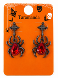 A pair of gothic Halloween earrings featuring black spider and cross charms with faceted red teardrop rhinestones, displayed on an orange cardboard backing card decorated with spiderwebs, bats, and the brand name 'Taramanda'.