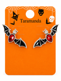 A pair of bat-shaped stud earrings with black wings, red oval stones, and small clear crystal accents, displayed on an orange Taramanda Halloween-themed backing card.