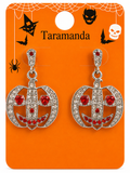 A pair of silver-toned Halloween dangle earrings with clear rhinestones and red crystal accents, displayed on an orange card printed with Halloween graphics and the brand name Taramanda.