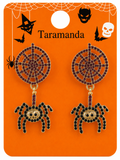 A pair of Halloween-themed spider drop earrings on an orange display card. The earrings feature gold-tone metal frames with black rhinestones forming spider bodies and web patterns, with a small purple crystal accent at the top of each spider.