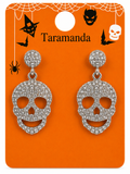 A pair of silver-toned skull drop earrings covered in clear rhinestones, displayed on an orange Halloween-themed card with the brand name Taramanda.
