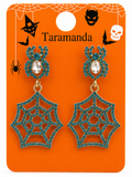 A pair of Halloween-themed dangle earrings on an orange display card. The earrings feature a spider head stud with a clear rhinestone center and a large spiderweb-shaped drop covered in teal blue rhinestones with gold-tone metal outlines.