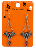 A pair of silver-tone bat drop earrings with dark red enamel accents, displayed on an orange Halloween-themed card labeled 'Taramanda'.