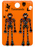 A pair of skeleton-shaped dangling earrings on an orange Halloween-themed display card. The earrings are black with many colorful rhinestones in red, blue, green, purple, and silver.