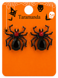 A pair of black spider-shaped stud earrings with faceted red crystal centers, displayed on an orange Halloween-themed backing card labeled 'Taramanda' with spider, bat, witch hat, devil mask, and skull graphics.