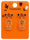 A pair of Taramanda brand Halloween dangle earrings on an orange display card. The earrings feature a black bow with an orange faceted crystal top and a dangling orange jack-o'-lantern pumpkin bucket charm with gold-tone trim and multicolor rhinestone accents.