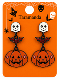 A pair of Halloween-themed dangle earrings displayed on an orange backing card. Each earring features a white skull stud, a black bat charm with red rhinestones, and a pumpkin charm with black facial details and small pink diamond accents.