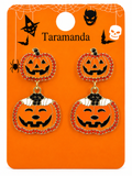 A pair of Halloween-themed dangle earrings displayed on an orange retail backing card. The earrings feature jack-o'-lantern faces outlined with red rhinestones, with one pumpkin charm decorated in orange, black, and white.
